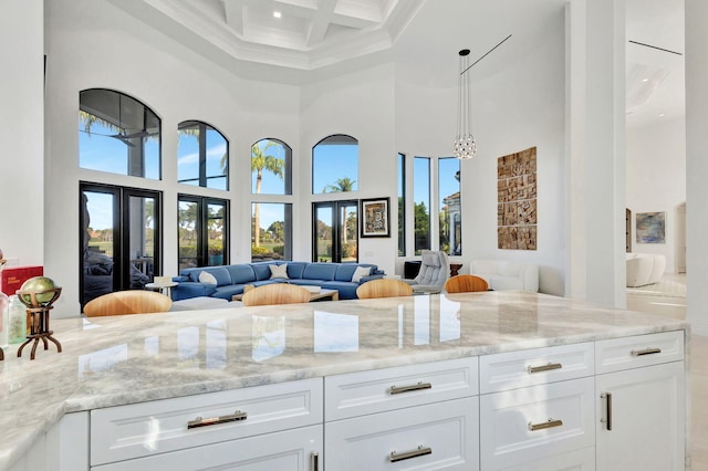 kitchen with white cabinets, a towering ceiling, light stone counters, and coffered ceiling