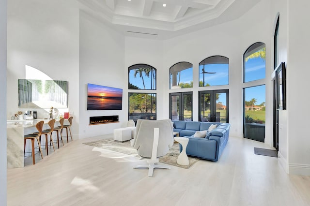 living room featuring beam ceiling, light hardwood / wood-style floors, a high ceiling, and coffered ceiling