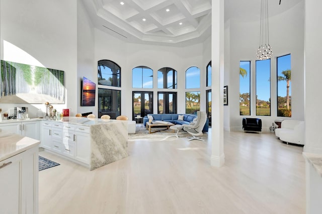 living room featuring coffered ceiling, a high ceiling, beamed ceiling, a notable chandelier, and light hardwood / wood-style floors