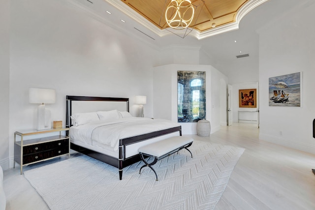 bedroom with a notable chandelier, light wood-type flooring, a high ceiling, and a tray ceiling