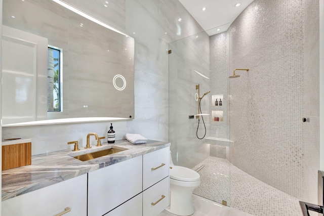 bathroom with toilet, a tile shower, tile walls, and vanity