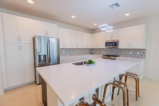 kitchen featuring pendant lighting, white cabinetry, stainless steel appliances, and a center island with sink