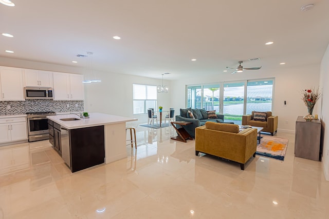 kitchen featuring hanging light fixtures, a center island with sink, appliances with stainless steel finishes, ceiling fan with notable chandelier, and white cabinets