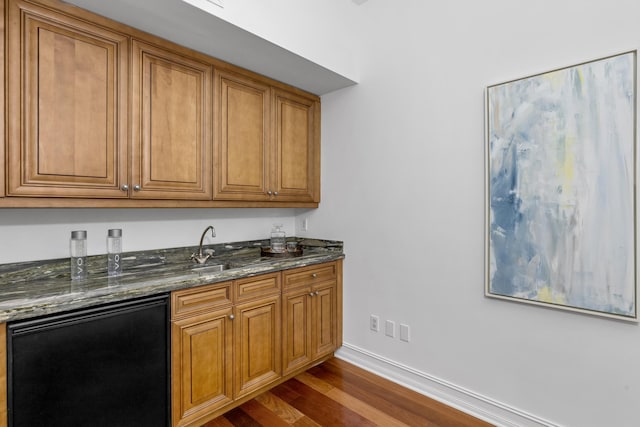 kitchen featuring refrigerator, dark stone countertops, wood-type flooring, and sink