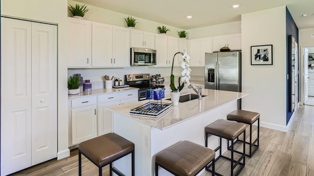 kitchen featuring a kitchen bar, appliances with stainless steel finishes, light wood-type flooring, and a kitchen island with sink