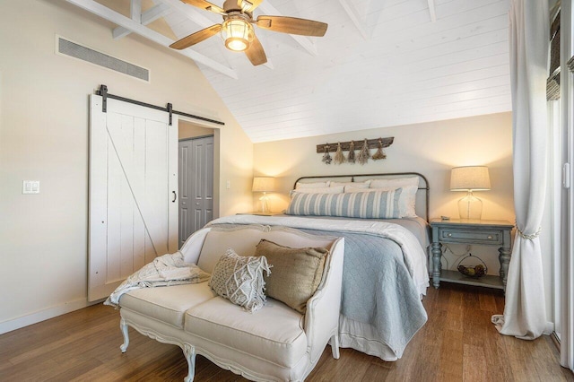 bedroom featuring lofted ceiling with beams, hardwood / wood-style flooring, ceiling fan, a barn door, and a closet