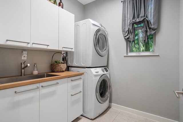 laundry room with sink, light tile patterned floors, cabinets, and stacked washer and clothes dryer