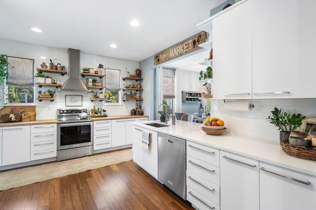 kitchen featuring white cabinets, wall chimney range hood, sink, dark hardwood / wood-style flooring, and stainless steel appliances