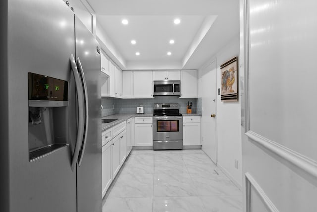 kitchen with sink, stainless steel appliances, a raised ceiling, backsplash, and white cabinets