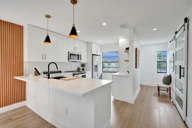 kitchen with kitchen peninsula, appliances with stainless steel finishes, sink, a barn door, and white cabinets