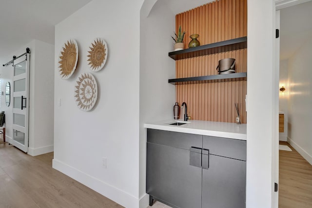 bar with a barn door, sink, and light hardwood / wood-style flooring