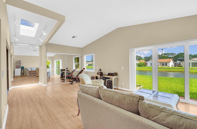 living room featuring a water view, lofted ceiling with skylight, light wood-type flooring, and track lighting