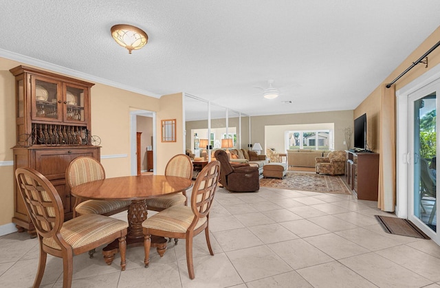 tiled dining space with ornamental molding, a textured ceiling, ceiling fan, and a healthy amount of sunlight