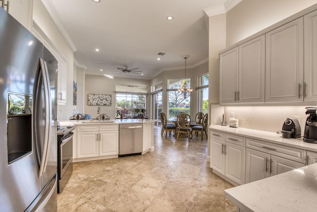 kitchen with sink, stainless steel appliances, pendant lighting, ceiling fan with notable chandelier, and ornamental molding