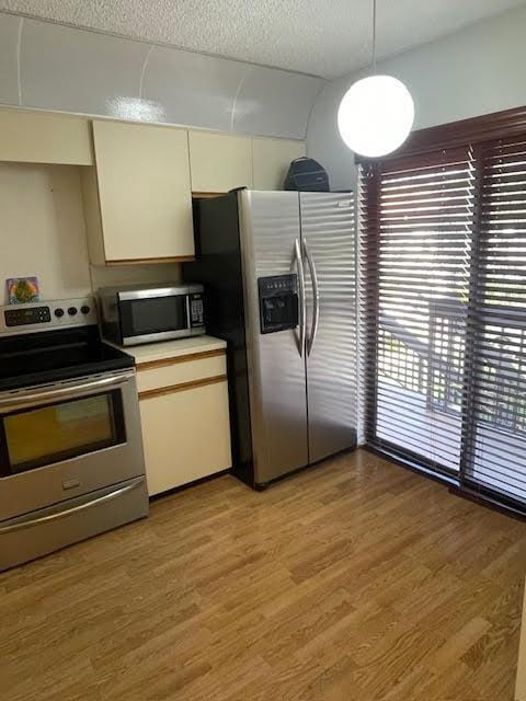 kitchen with a textured ceiling, light hardwood / wood-style floors, decorative light fixtures, and appliances with stainless steel finishes