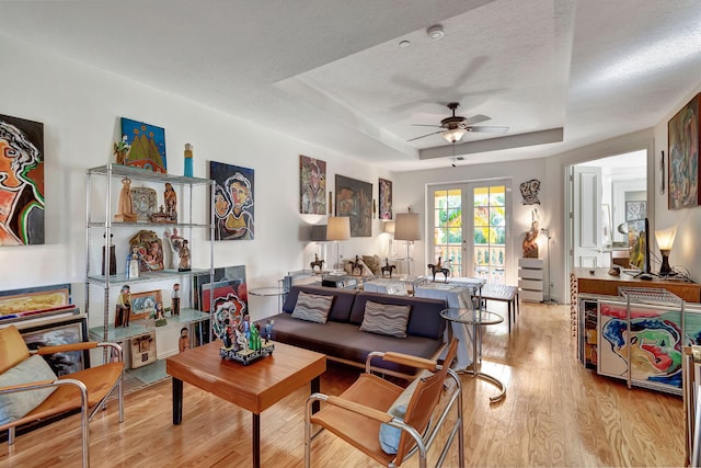 living room featuring ceiling fan, french doors, light hardwood / wood-style floors, a textured ceiling, and a tray ceiling