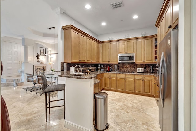 kitchen with a kitchen bar, kitchen peninsula, decorative columns, dark stone counters, and stainless steel appliances