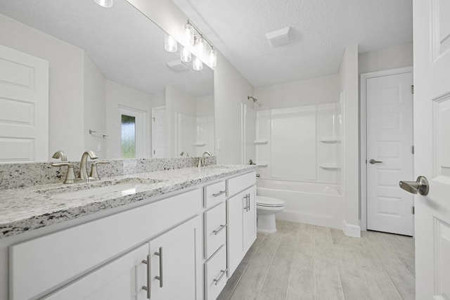 full bathroom featuring vanity, bathtub / shower combination, toilet, and a textured ceiling