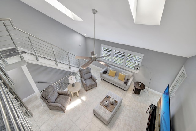 living room featuring tile patterned flooring, ceiling fan, high vaulted ceiling, and a skylight