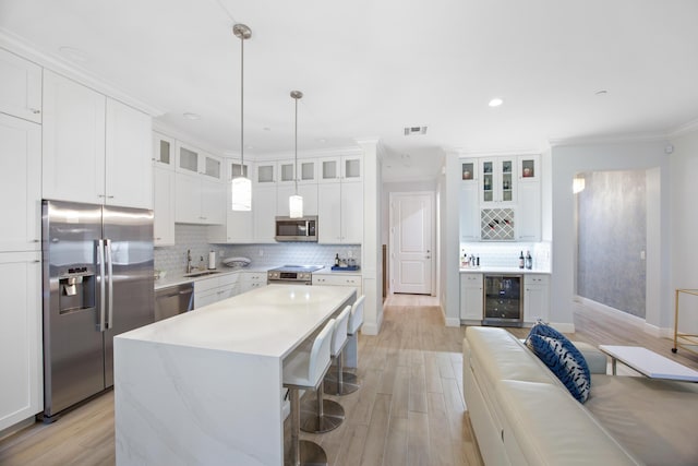 kitchen with a kitchen island, beverage cooler, crown molding, white cabinets, and appliances with stainless steel finishes