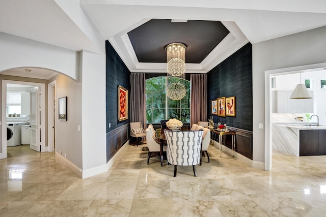 dining room with a raised ceiling, sink, an inviting chandelier, and washer / dryer