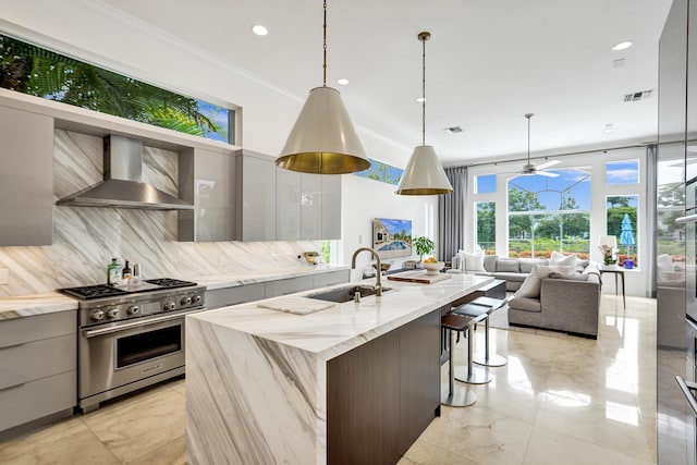 kitchen featuring backsplash, high end stove, wall chimney range hood, sink, and decorative light fixtures