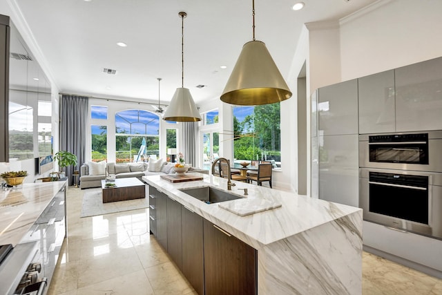 kitchen featuring pendant lighting, a spacious island, sink, light stone countertops, and ornamental molding