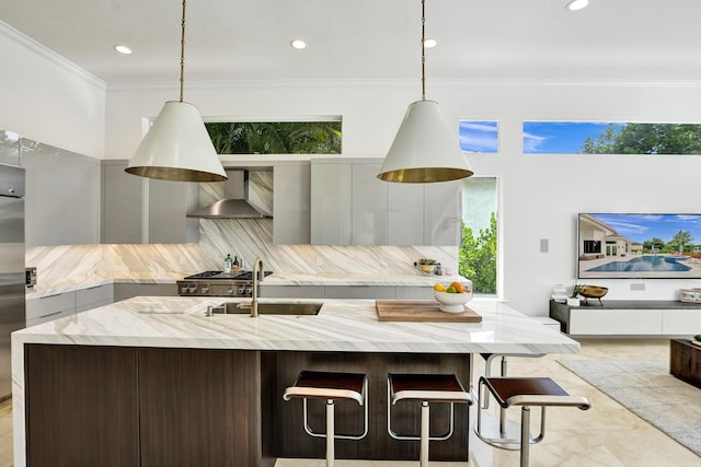 kitchen with pendant lighting, light stone counters, wall chimney range hood, and backsplash