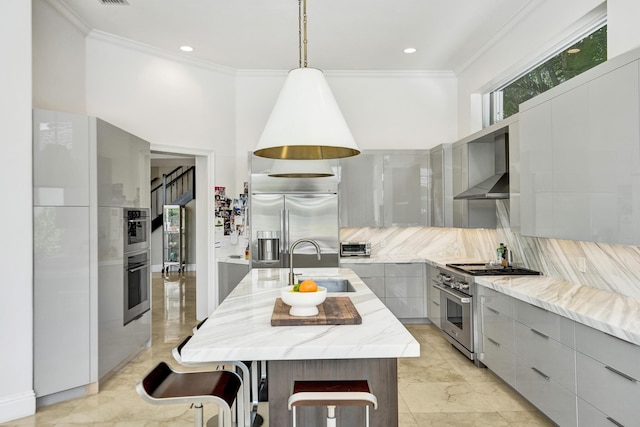 kitchen with appliances with stainless steel finishes, a kitchen island with sink, sink, wall chimney range hood, and gray cabinets