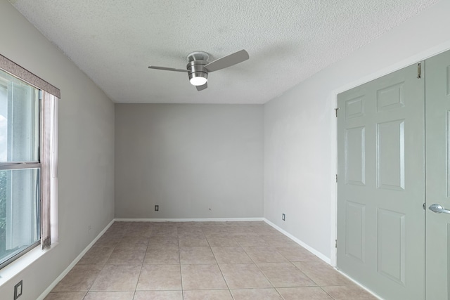 empty room featuring light tile patterned floors, a textured ceiling, ceiling fan, and a healthy amount of sunlight