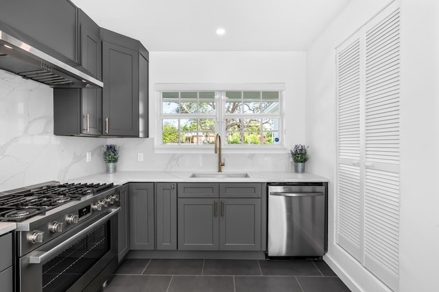 kitchen featuring dark tile patterned floors, wall chimney exhaust hood, stainless steel appliances, sink, and gray cabinets