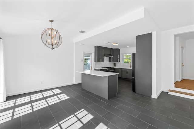 kitchen with ventilation hood, appliances with stainless steel finishes, decorative light fixtures, a notable chandelier, and dark tile patterned flooring