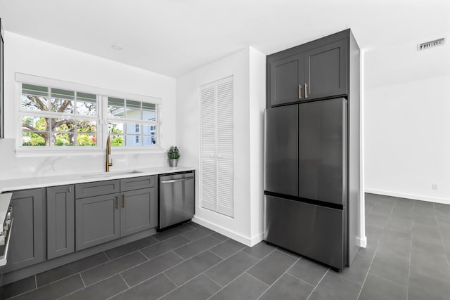 kitchen with sink, dark tile patterned flooring, appliances with stainless steel finishes, and gray cabinetry