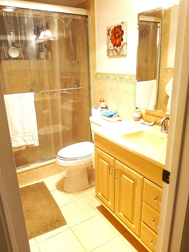 bathroom with tile patterned floors, vanity, a shower with door, tile walls, and toilet