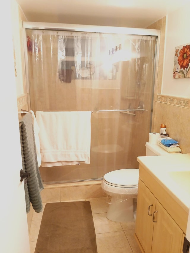 bathroom featuring tile patterned flooring, an enclosed shower, toilet, vanity, and tile walls