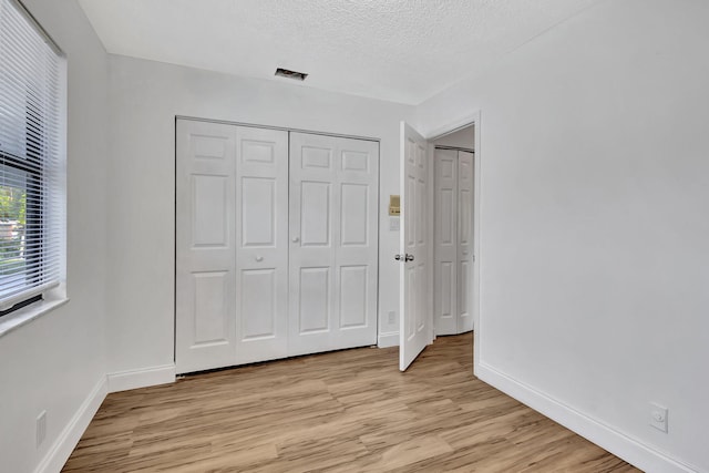 unfurnished bedroom with light hardwood / wood-style floors, a textured ceiling, and a closet