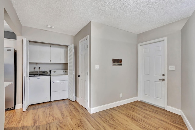 laundry area featuring washer and clothes dryer, cabinets, a textured ceiling, and light wood-type flooring