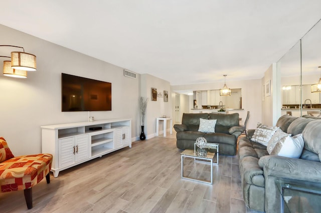 living area featuring visible vents, light wood-style flooring, and baseboards