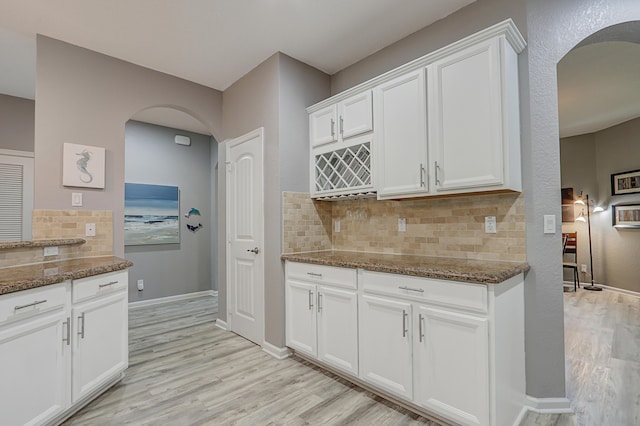 kitchen with stone countertops, decorative light fixtures, white cabinetry, stainless steel fridge, and a center island with sink