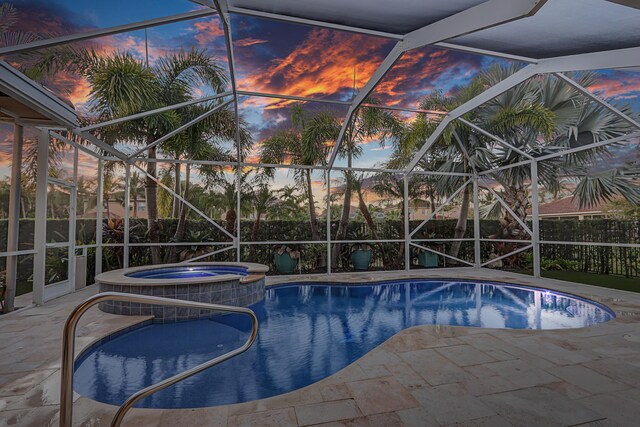 pool at dusk with an in ground hot tub, a lanai, and a patio