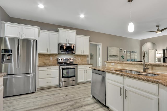 kitchen featuring white cabinets, decorative backsplash, stainless steel appliances, light stone countertops, and light wood-type flooring