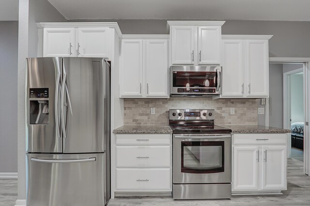 kitchen with backsplash, white cabinets, light wood-type flooring, and dark stone counters