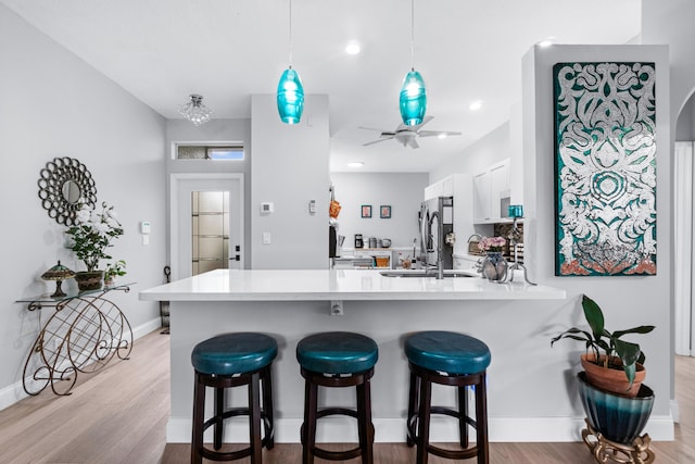 kitchen with white cabinetry, ceiling fan, kitchen peninsula, light hardwood / wood-style floors, and a kitchen bar