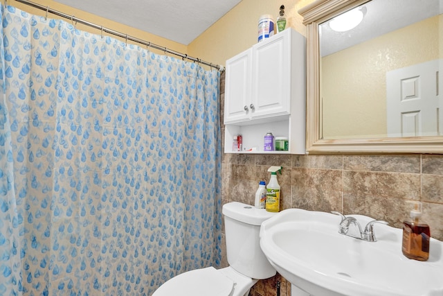 bathroom with a textured ceiling, toilet, curtained shower, and sink