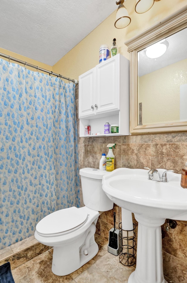 bathroom with a textured ceiling, a shower with curtain, toilet, and tile walls