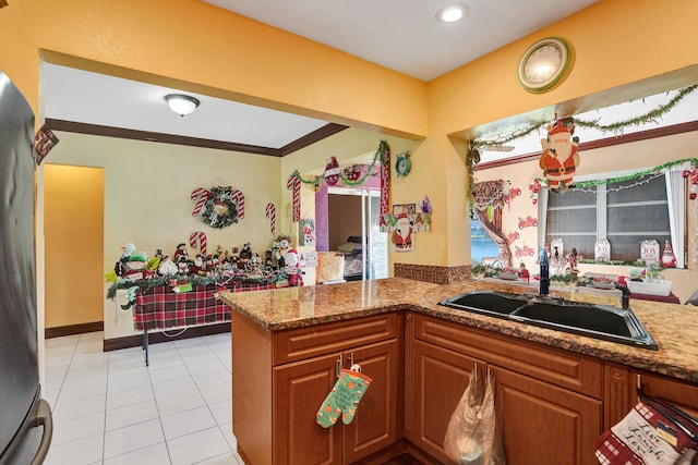 kitchen featuring crown molding, stone countertops, light tile patterned flooring, kitchen peninsula, and stainless steel refrigerator