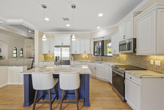 kitchen with appliances with stainless steel finishes, ceiling fan, decorative light fixtures, white cabinets, and a center island