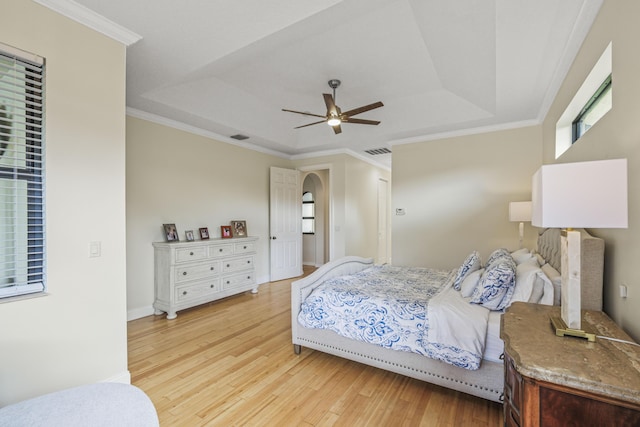 bedroom with ceiling fan, a raised ceiling, ornamental molding, and light hardwood / wood-style flooring