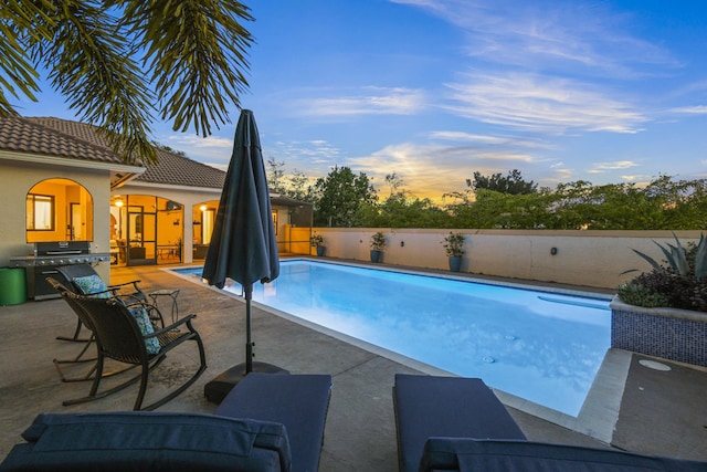 pool at dusk featuring a patio and grilling area