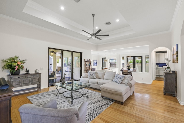 living room with light hardwood / wood-style flooring, a raised ceiling, a wealth of natural light, and crown molding